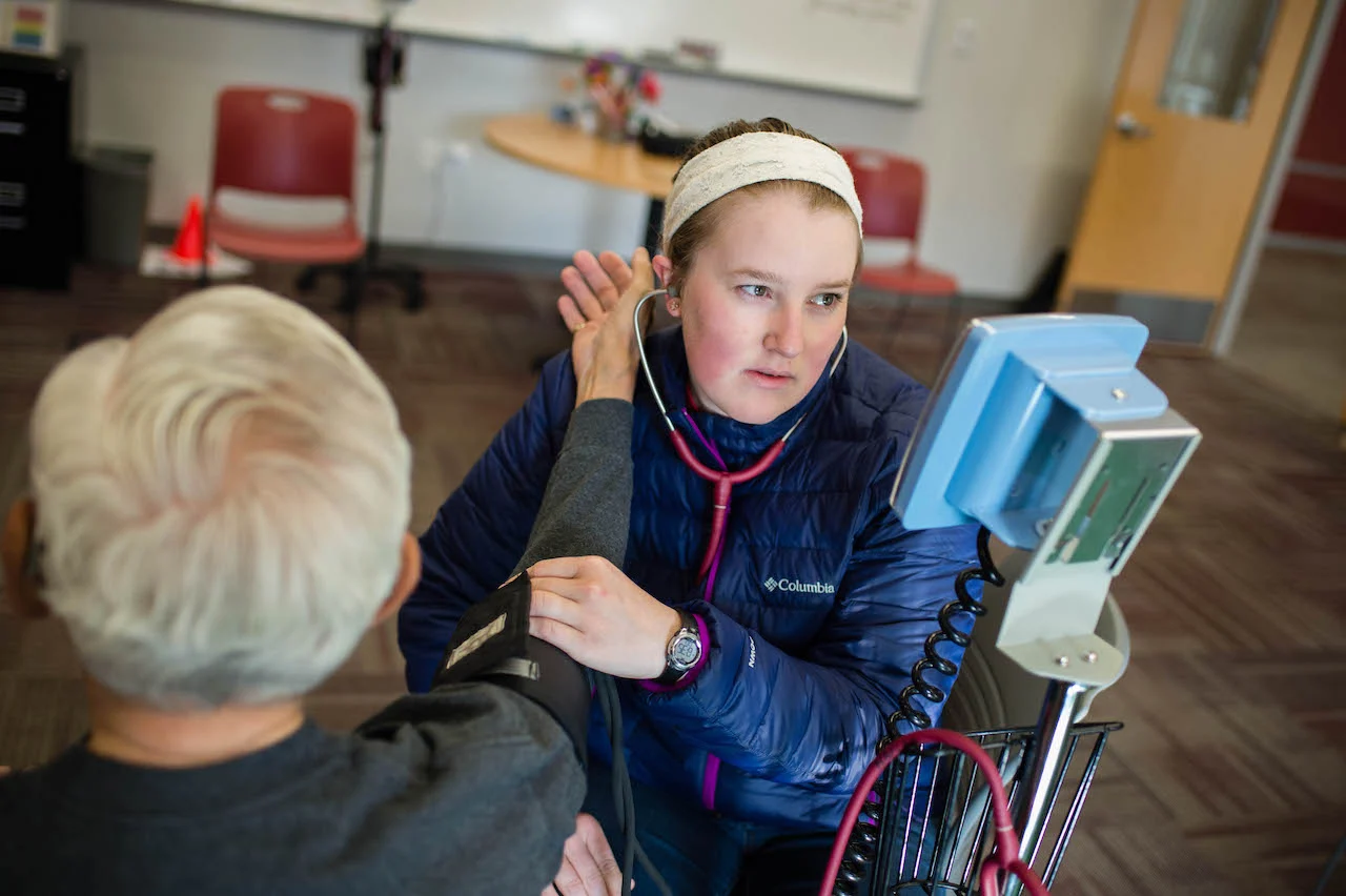 A student takes a community member's blood pressure.