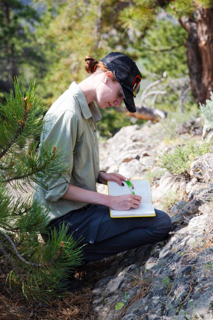 A geology student writes in a notebook while examining some rock during a geology field camp.