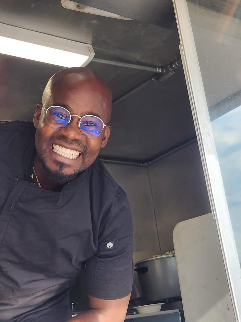 Jermaine smiles in the window of his Jamaican restaurant.