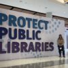Taylor poses in front of a "Protect Public Libraries" sign.
