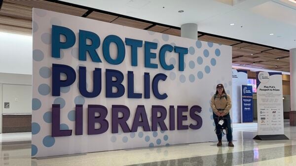 Taylor poses in front of a "Protect Public Libraries" sign.