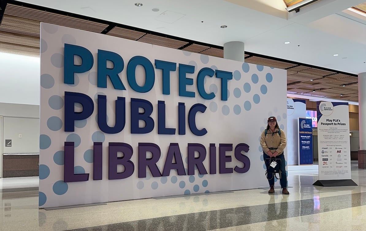 Taylor poses in front of a "Protect Public Libraries" sign.