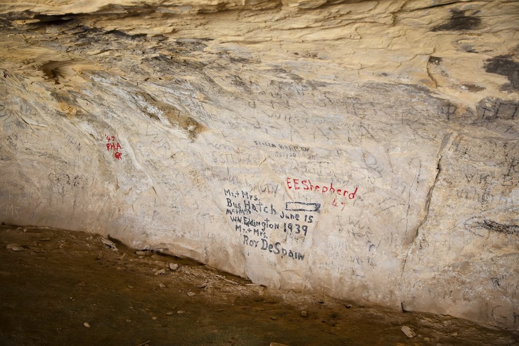 A rock wall inside a cave is covered with numerous inscriptions and markings, including some in red ink, dated to 1939.